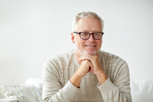 middle aged man sitting on coach in beige jumper resting head on hands