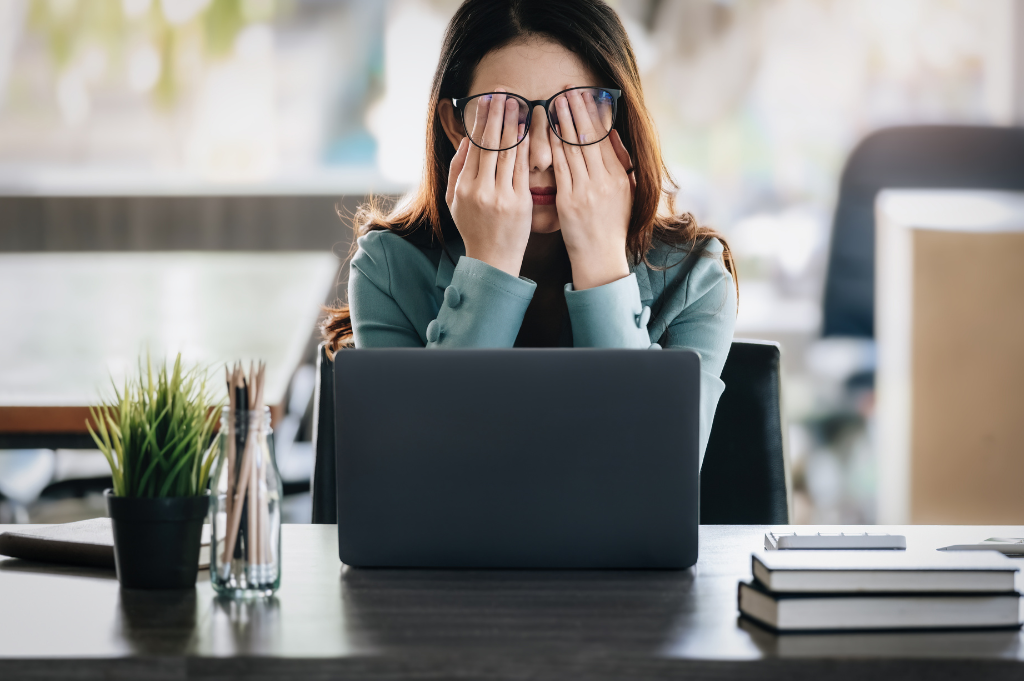 A woman sitting at her desk holding hands over eyes feeling burnt out