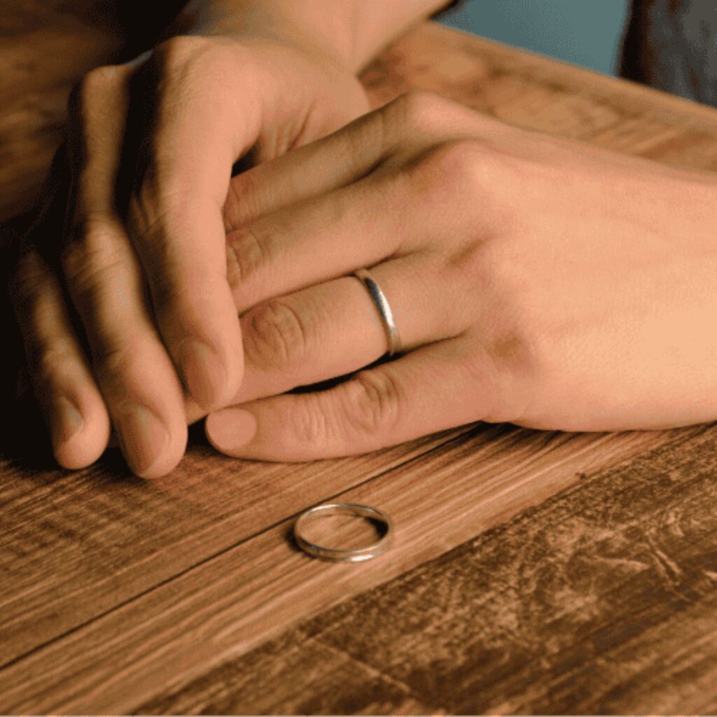 Person wearing a wedding ring with their partner's wedding ring beside them, in need of separation and divorce therapy